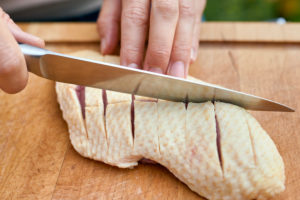 Frauenhände mit Kochmesser ritzen die Haut einer Entenbrustein, Holzbrett Frauenhände mit Kochmesser ritzen die Haut einer Entenbrustein, Holzbrett